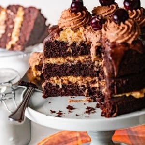German chocolate cake with coconut pecan frosting on a cake stand with a cake server with a few slices taken out.