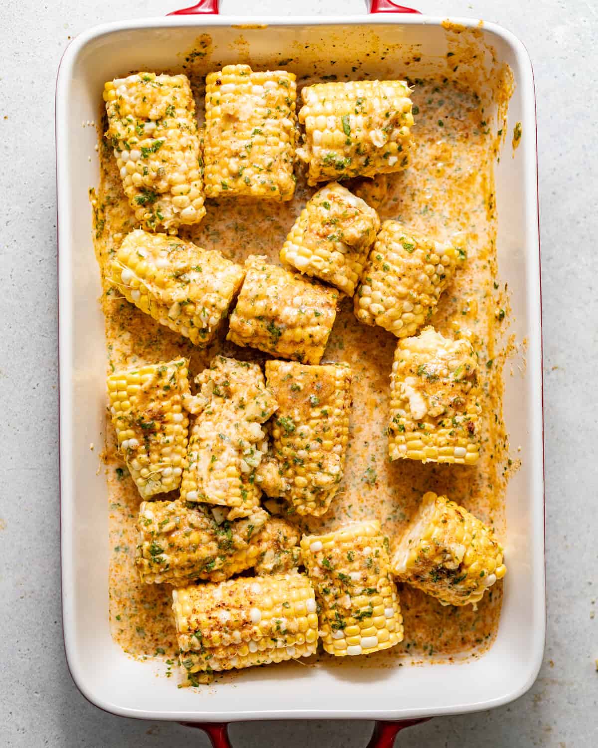 corn on the cob in a baking dish covered in garlic butter.