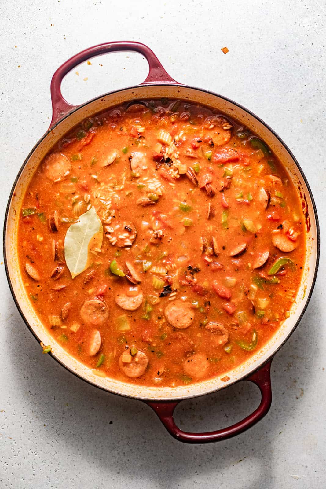 sausage, veggies, rice, and broth added to the skillet along with a bay leaf on top to simmer until the rice is fully cooked.