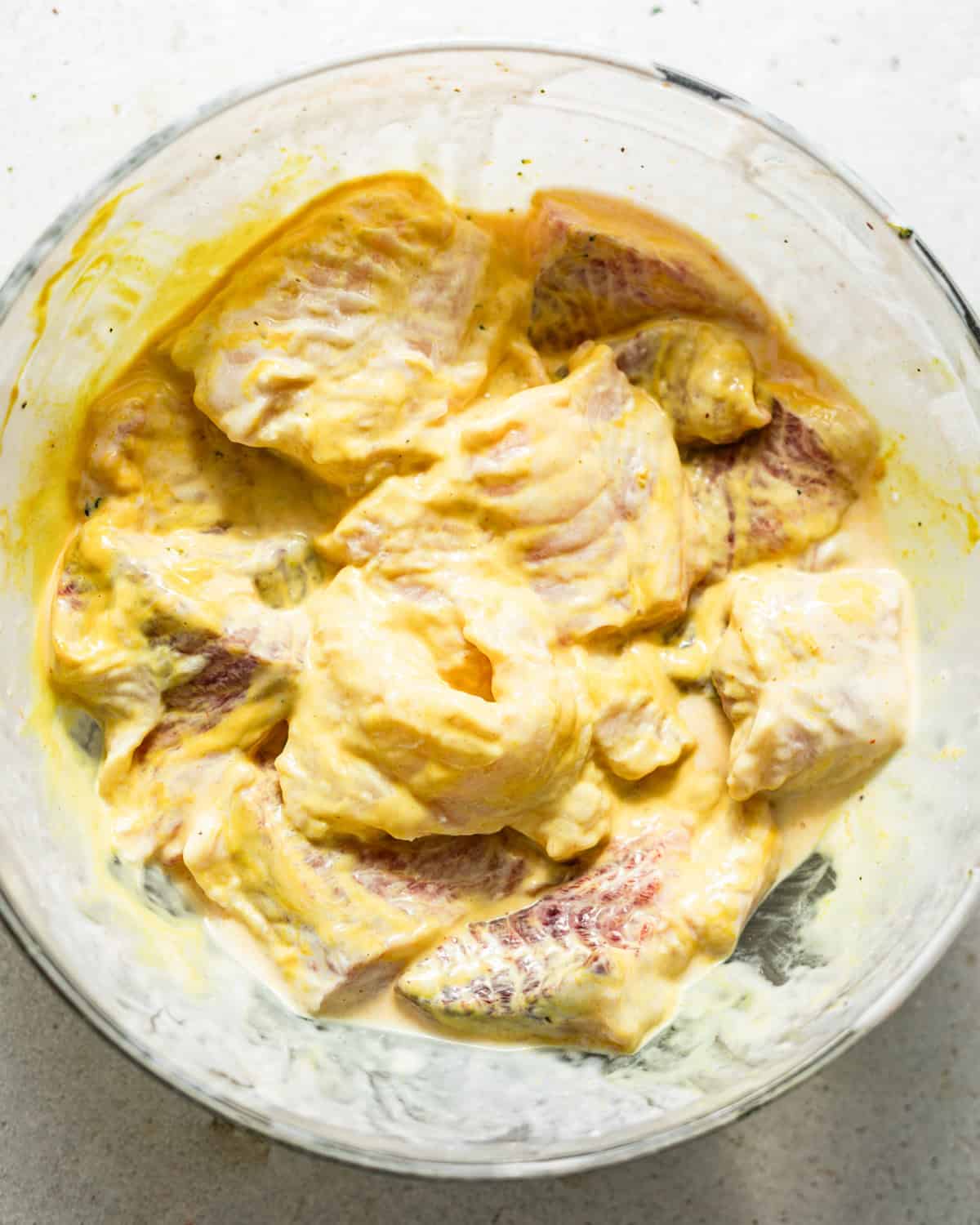 catfish nuggets in a bowl covered in seasonings and yellow mustard.