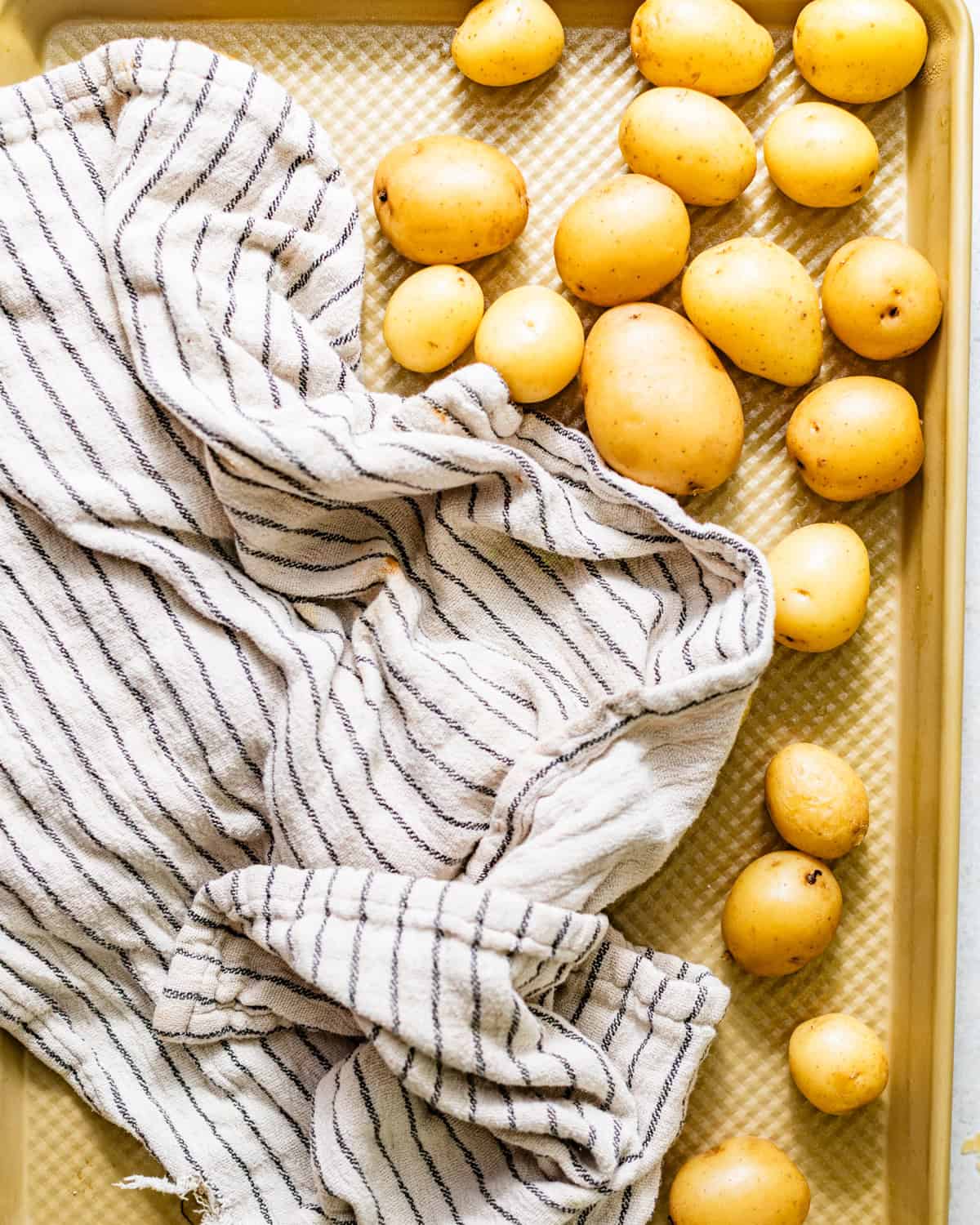 cooked baby potatoes on a baking sheet being dried with a kitchen towel.