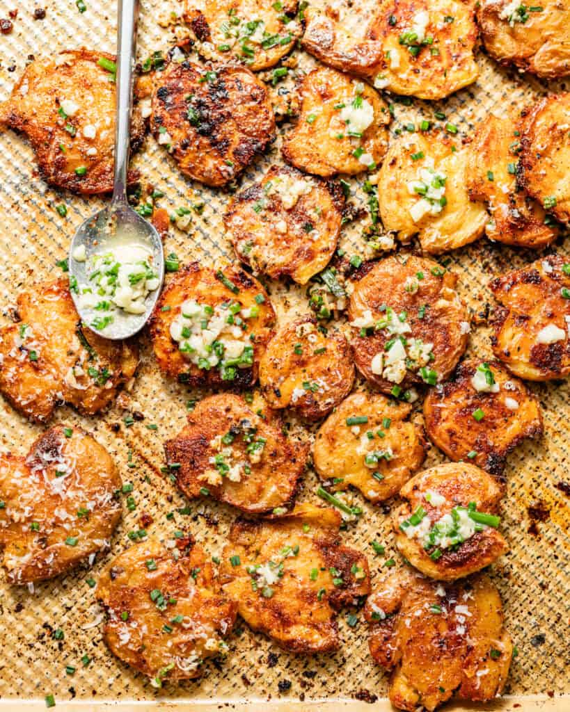garlic butter poured on top of the smashed potatoes on a baking sheet.
