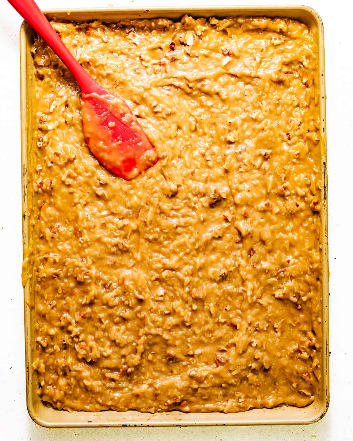 coconut pecan frosting spread out onto a baking sheet to cool and set.
