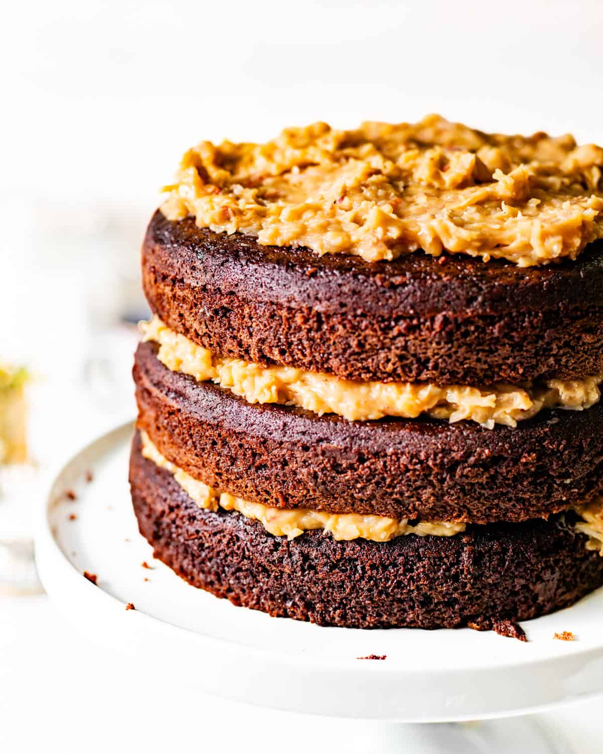 german chocolate cake on a cake stand with coconut pecan frosting between each layer.
