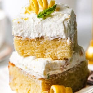 lemon sheet cake slices stacked on top of each other topped with lemon curls and a fresh mint leaf for garnish.
