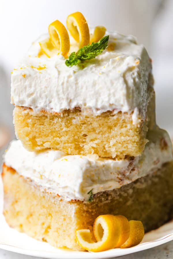 lemon sheet cake slices stacked on top of each other topped with lemon curls and a fresh mint leaf for garnish.
