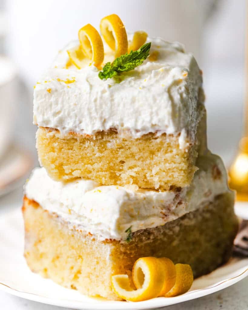 lemon sheet cake slices stacked on top of each other topped with lemon curls and a fresh mint leaf for garnish.