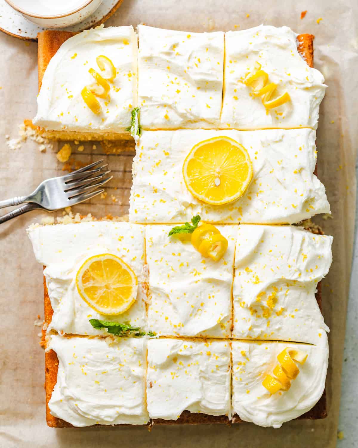 lemon sheet cake on a wire rack with lemon cream cheese frosting and fresh lemon zest and slices on top.