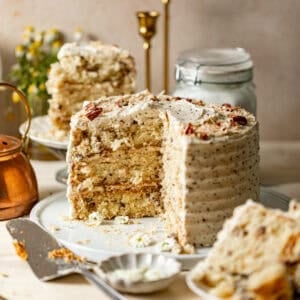 Italian cream layer cake with a slice removed, topped with chopped pecans and shredded coconut.