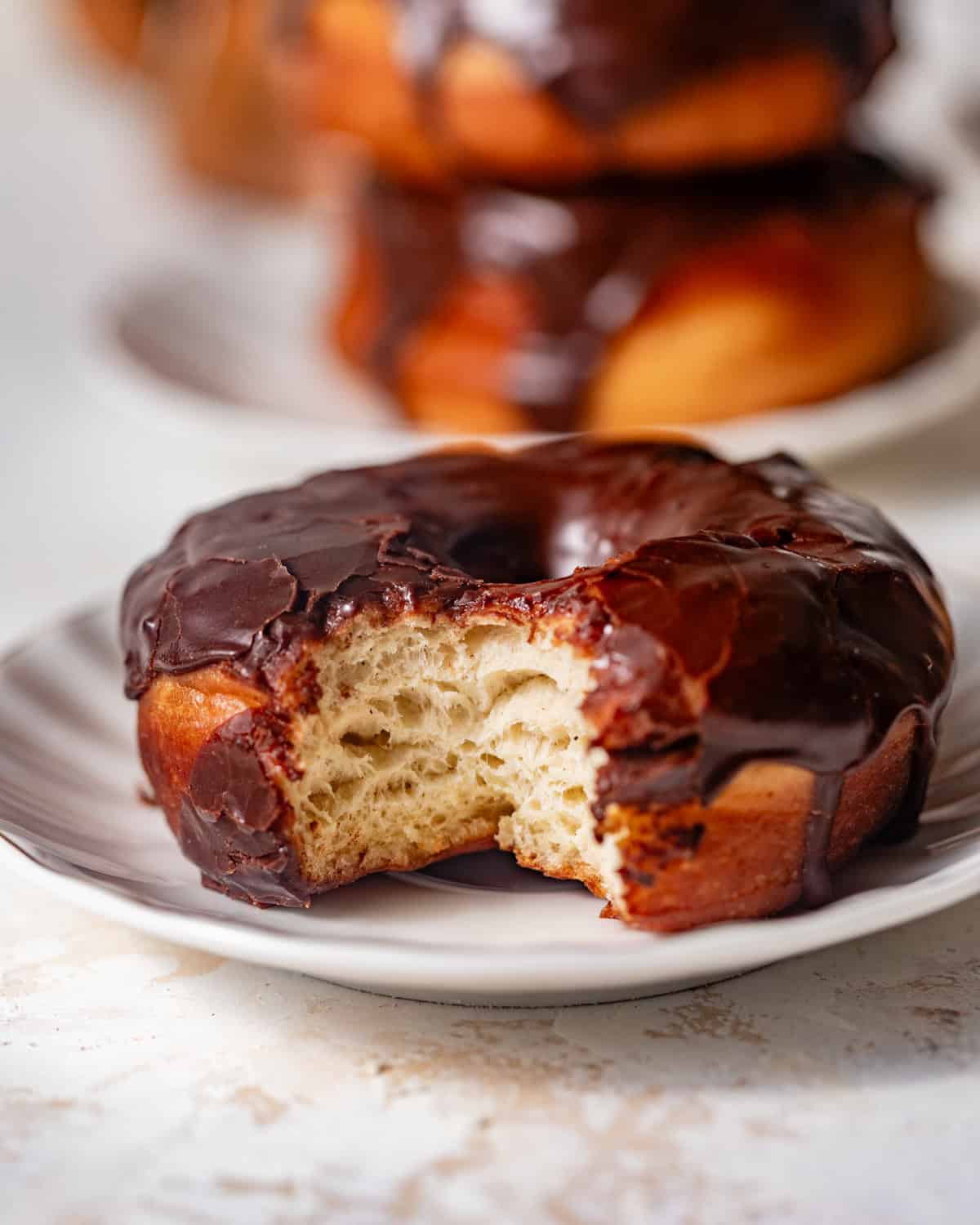 Chocolate glazed donut on a plate with a bite taken out, showing the soft interior.