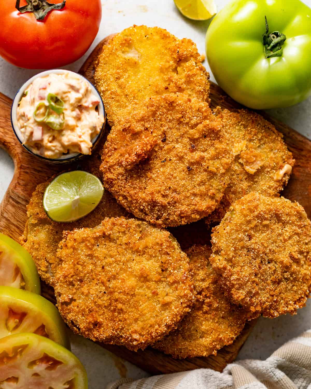 fried green tomatoes on a serving board with a small bowl of pimento cheese and a lime wedge on the side.