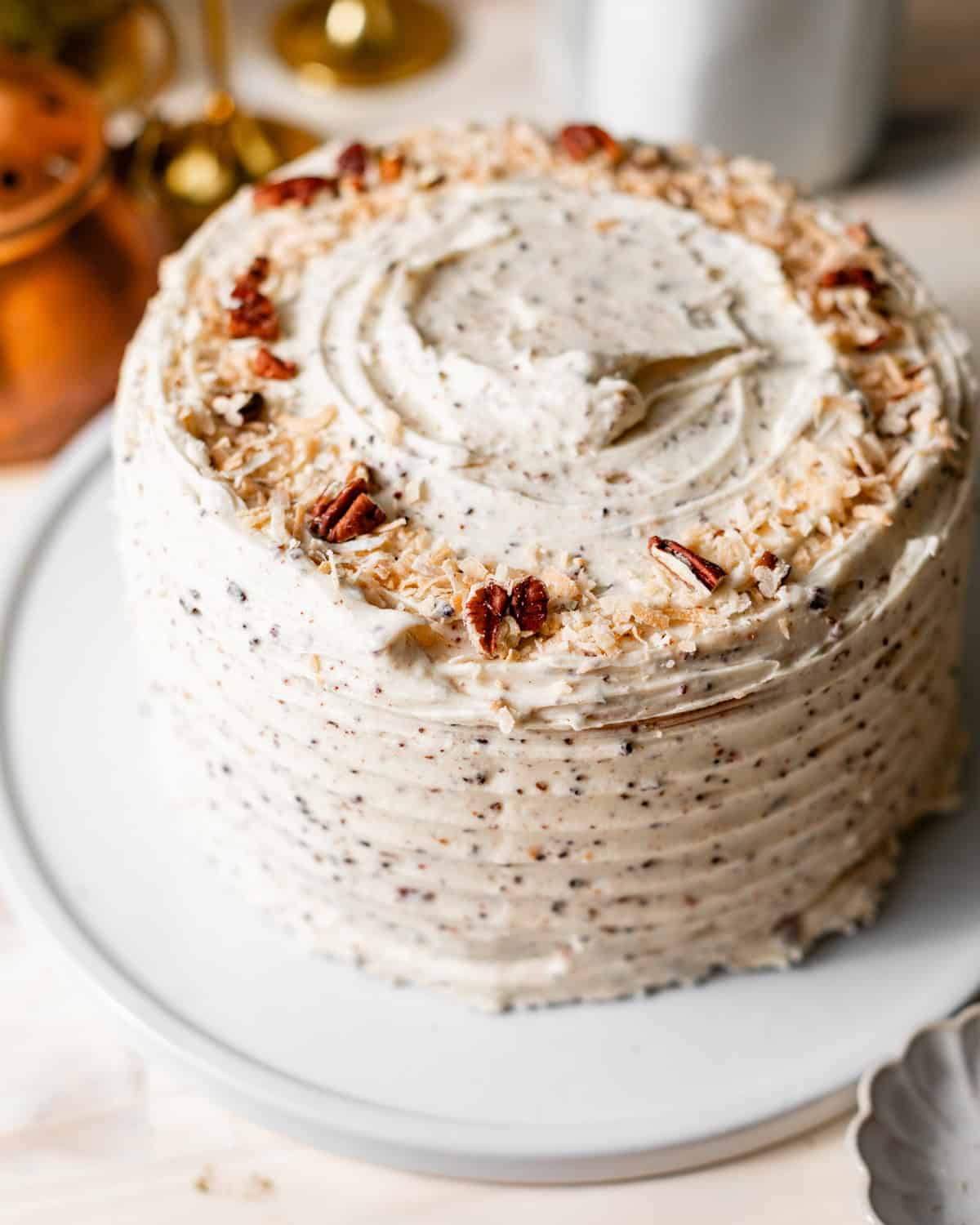 Italian cream cake assembled on a cake plate and topped with toasted coconut shreds and pecans.