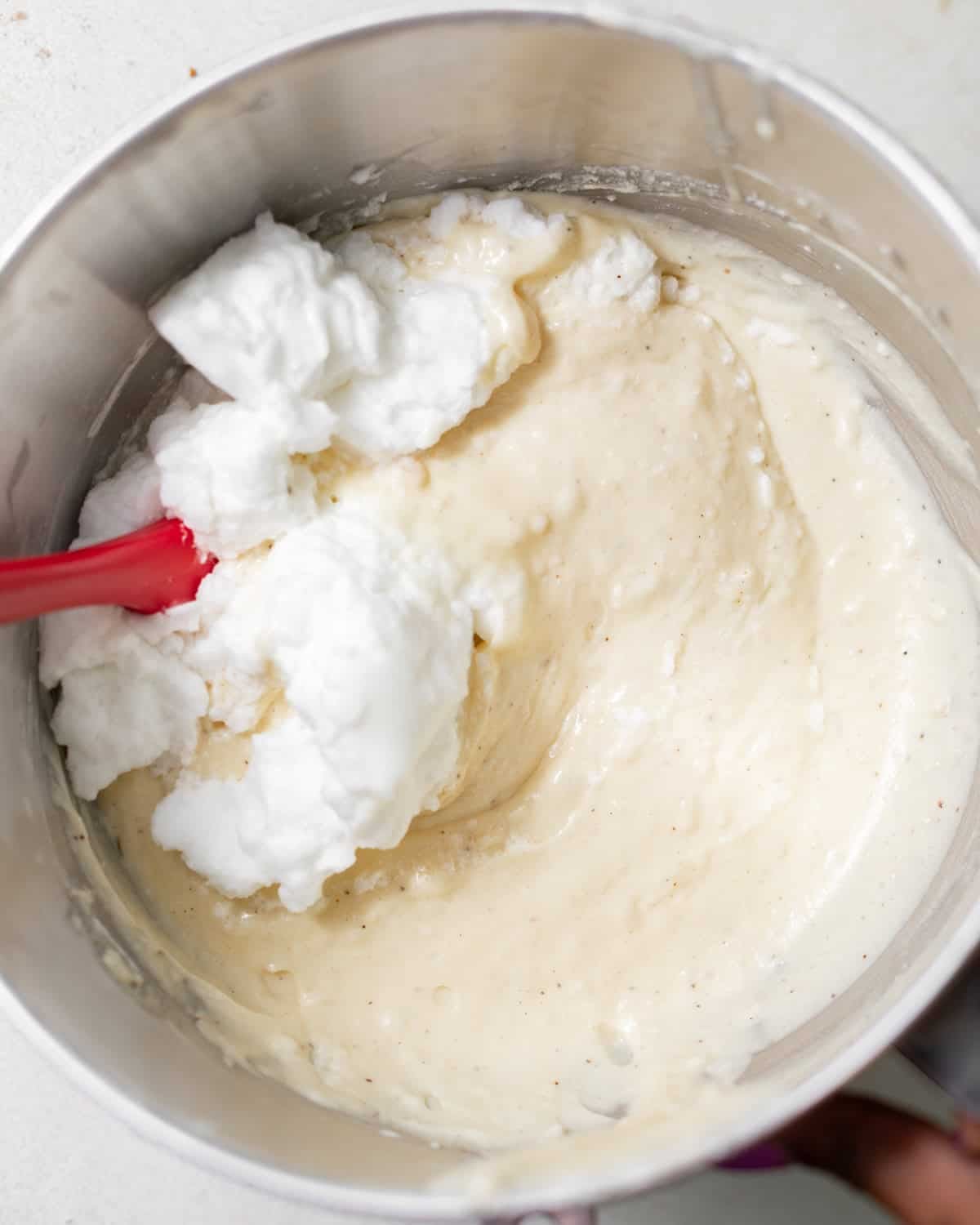 Whipped egg whites being folded gently into Italian cream cake batter.