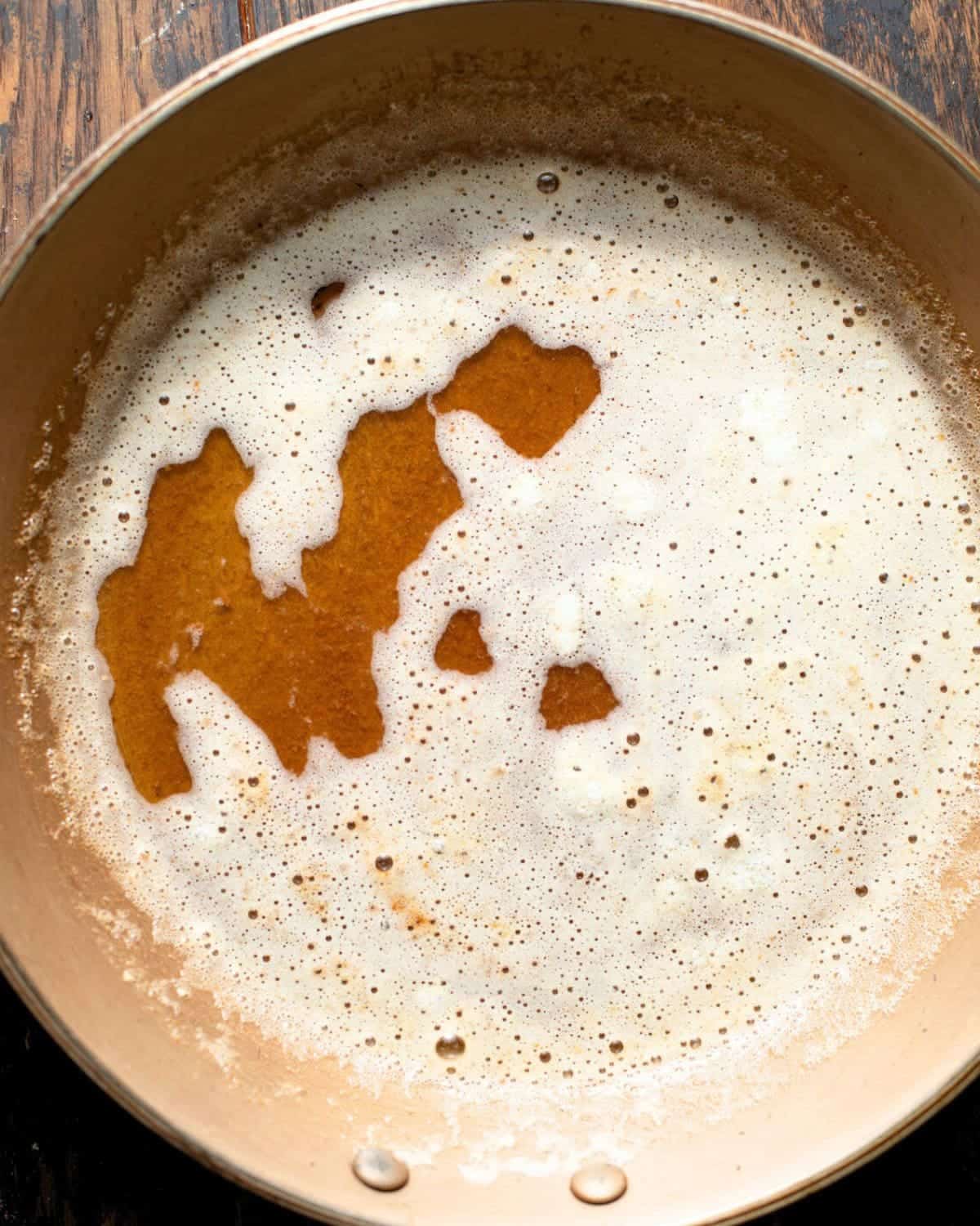 Brown butter and toasted milk solids foaming in a saucepan.