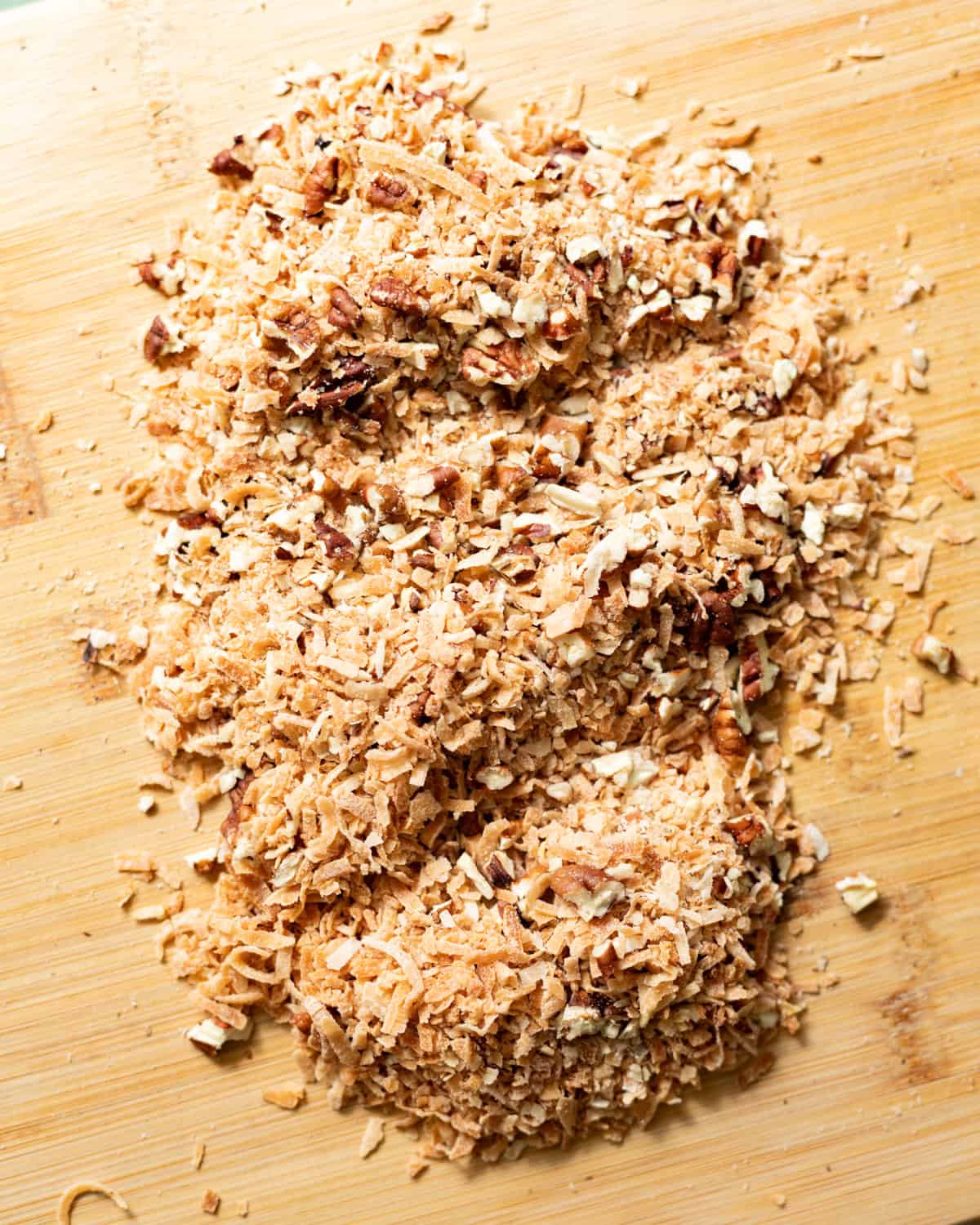 Finely chopped toasted coconut and pecans on a wooden cutting board.