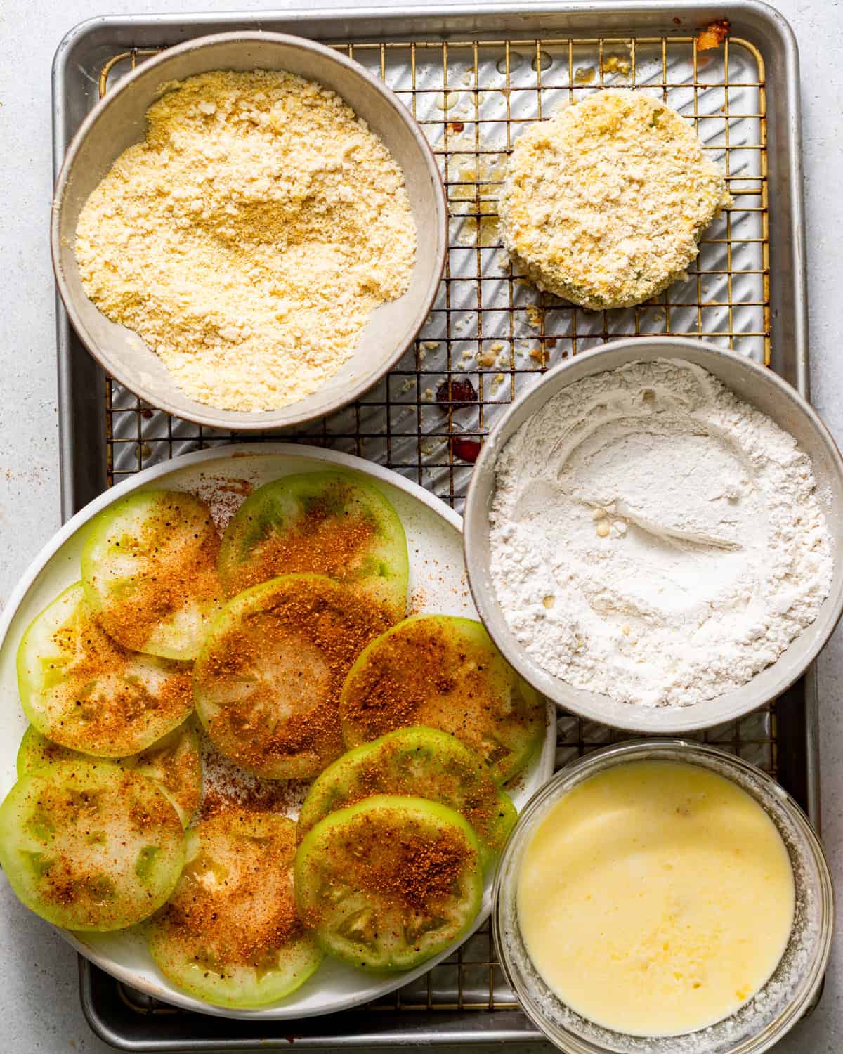breading station set up on a baking sheet - a bowl with buttermilk and eggs whisked together, another bowl with just flour, and another bowl with cornmeal and breadcrumbs mixed together.