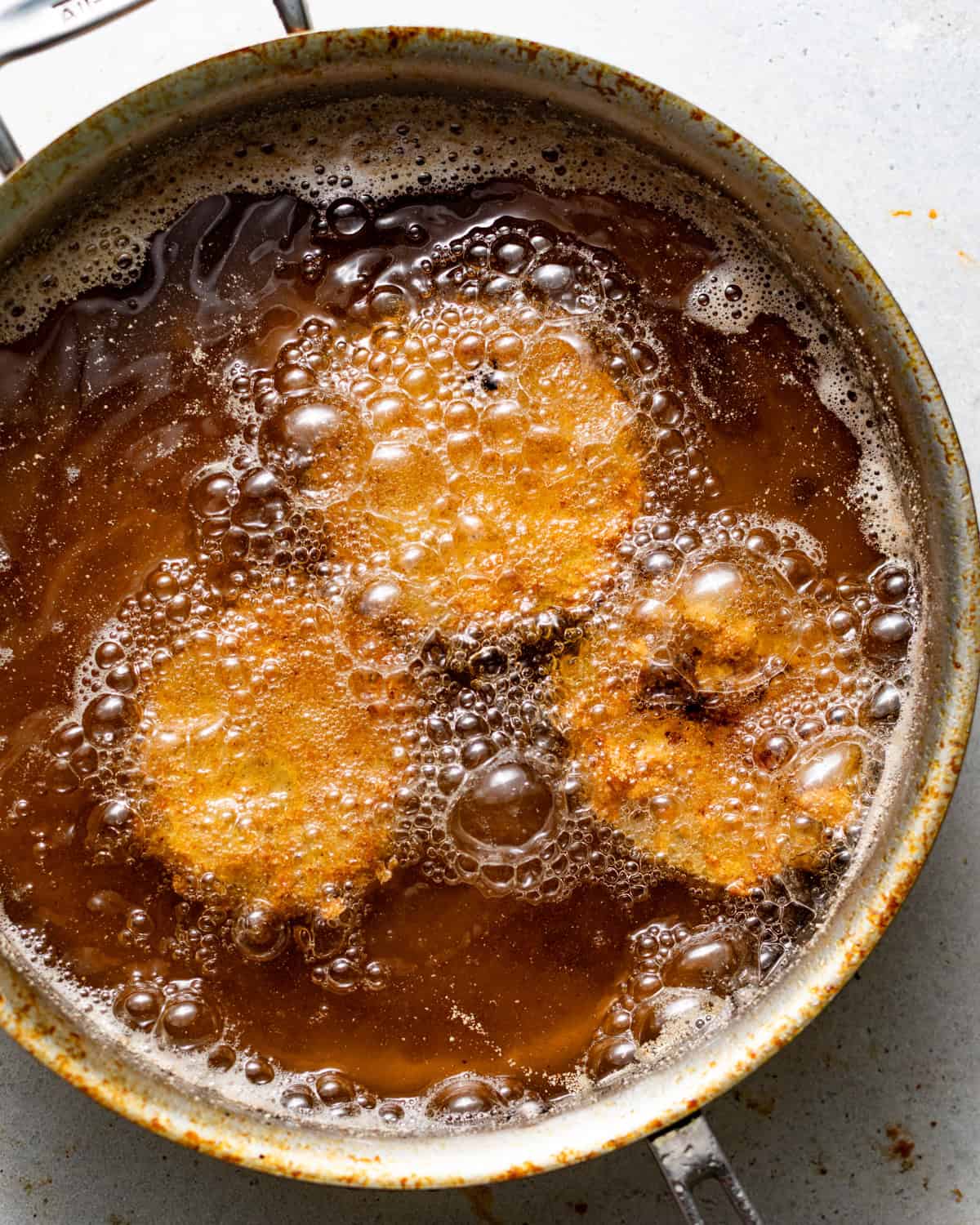 breaded green tomato slices frying in a skillet.