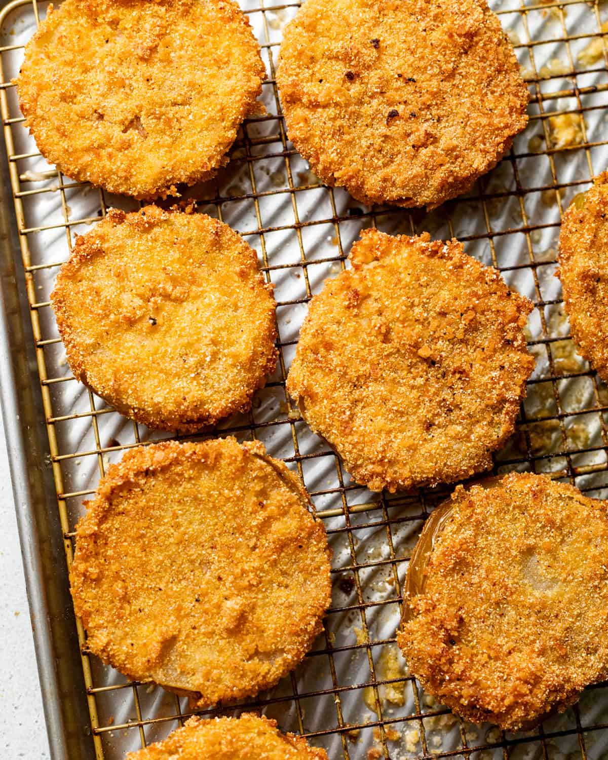 fried green tomatoes resting on a wire rack after frying.
