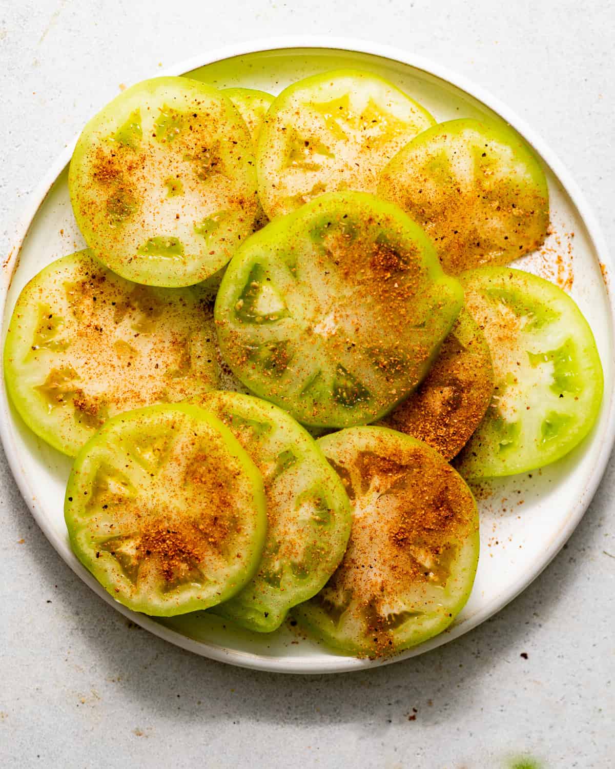 sliced green tomatoes on a plate sprinkled with Cajun seasoning.