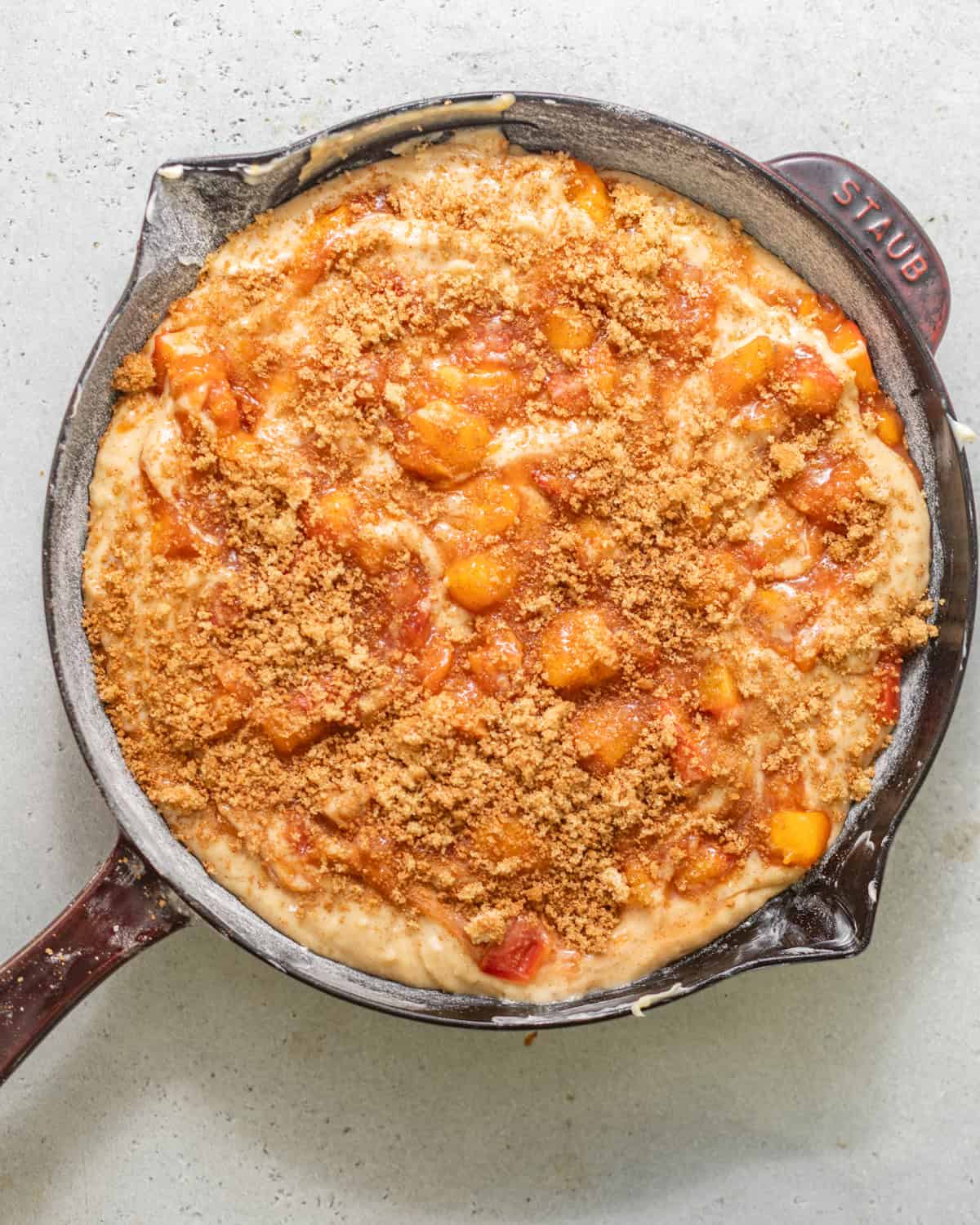 cake batter in a skillet with peach filling swirled throughout and topped with a brown sugar crunch topping.