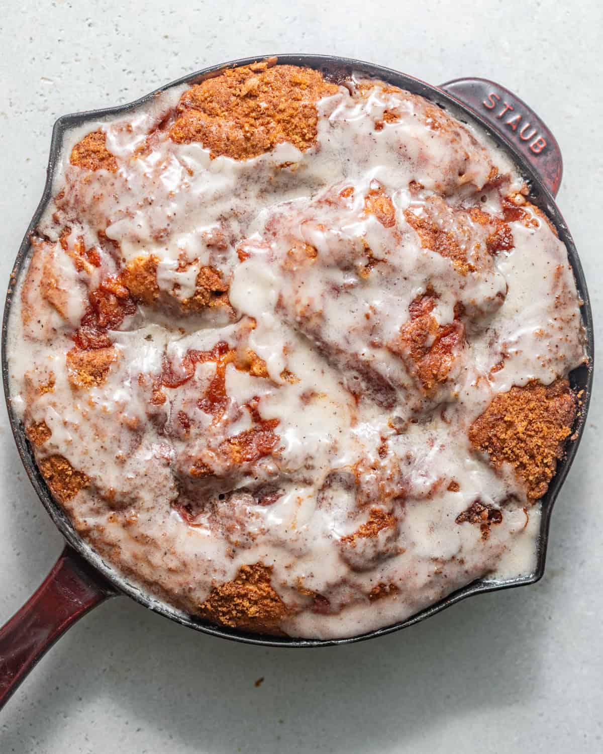 baked peach fritter cake in a skillet topped with vanilla bean glaze.