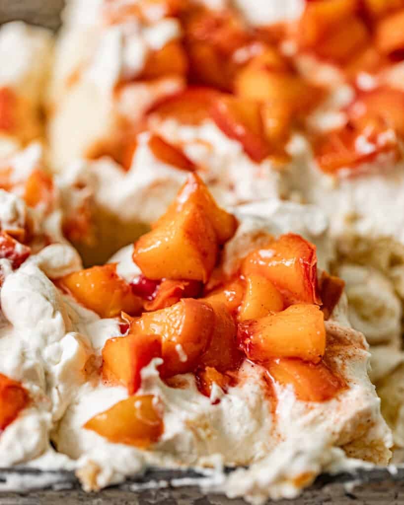 peach tres leches in a baking dish topped with whipped cream and peach cobbler topping.