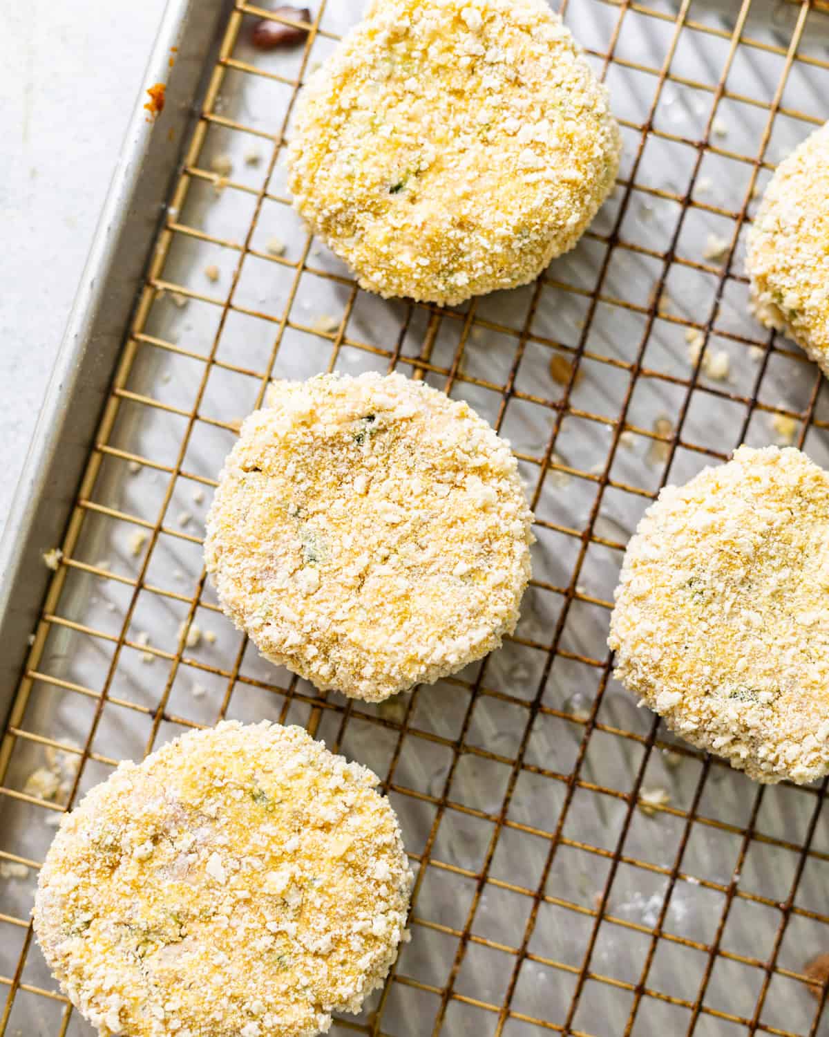 Uncooked salmon croquettes coated in breadcrumbs and cornmeal on a wire rack.