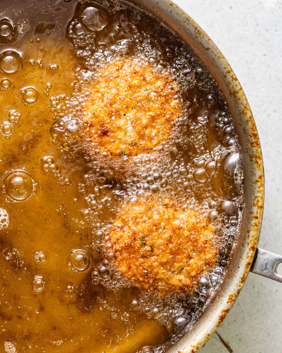 Breaded salmon croquettes frying in hot oil until golden brown.