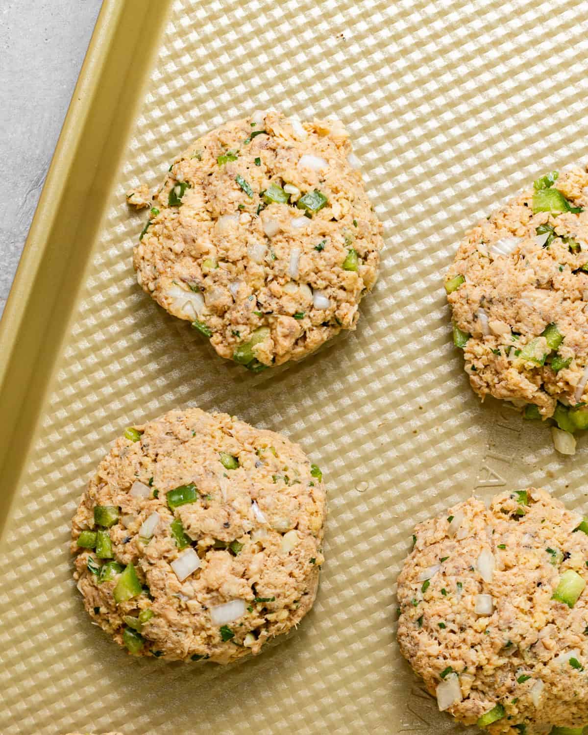 Uncooked salmon croquettes shaped into patties with diced bell pepper, onion, and parsley.