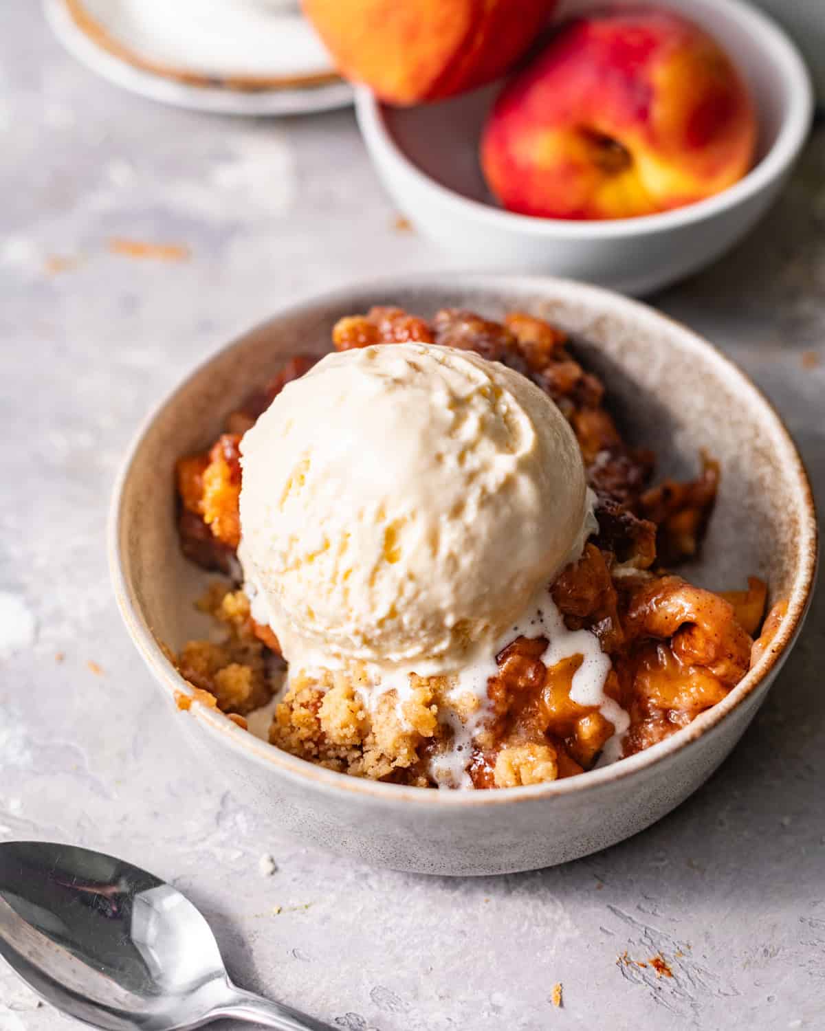 peach cobbler cinnamon roll bites in a bowl topped with ice cream.