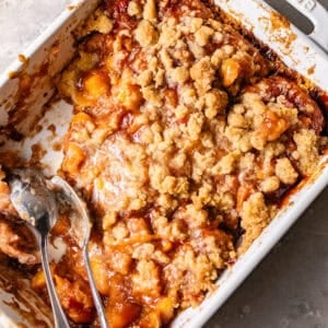 peach cobbler cinnamon roll bites in a baking dish with a spoon.