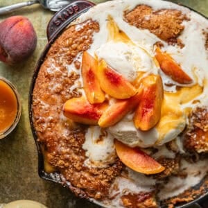 peach fritter cake in a skillet topped with ice cream and fresh peaches.