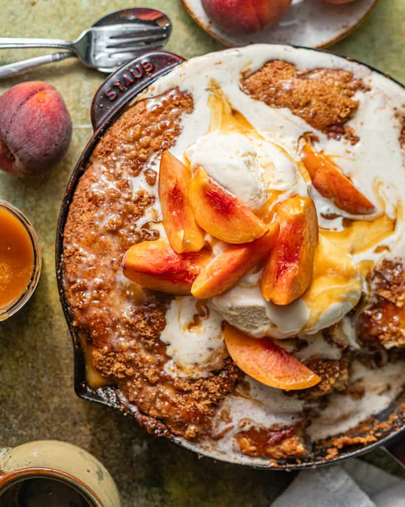 peach fritter cake in a skillet topped with ice cream and fresh peaches.