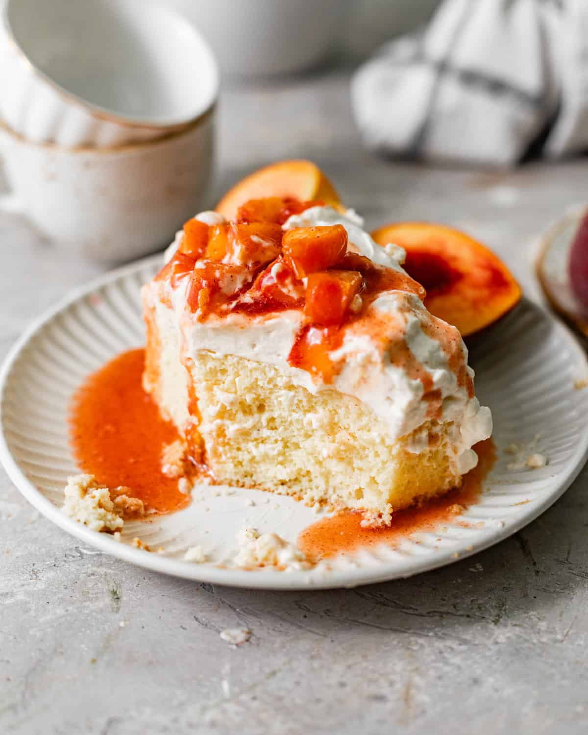 a slice of peach tres leches on a plate with a bite taken out so that you can see the texture of the cake.
