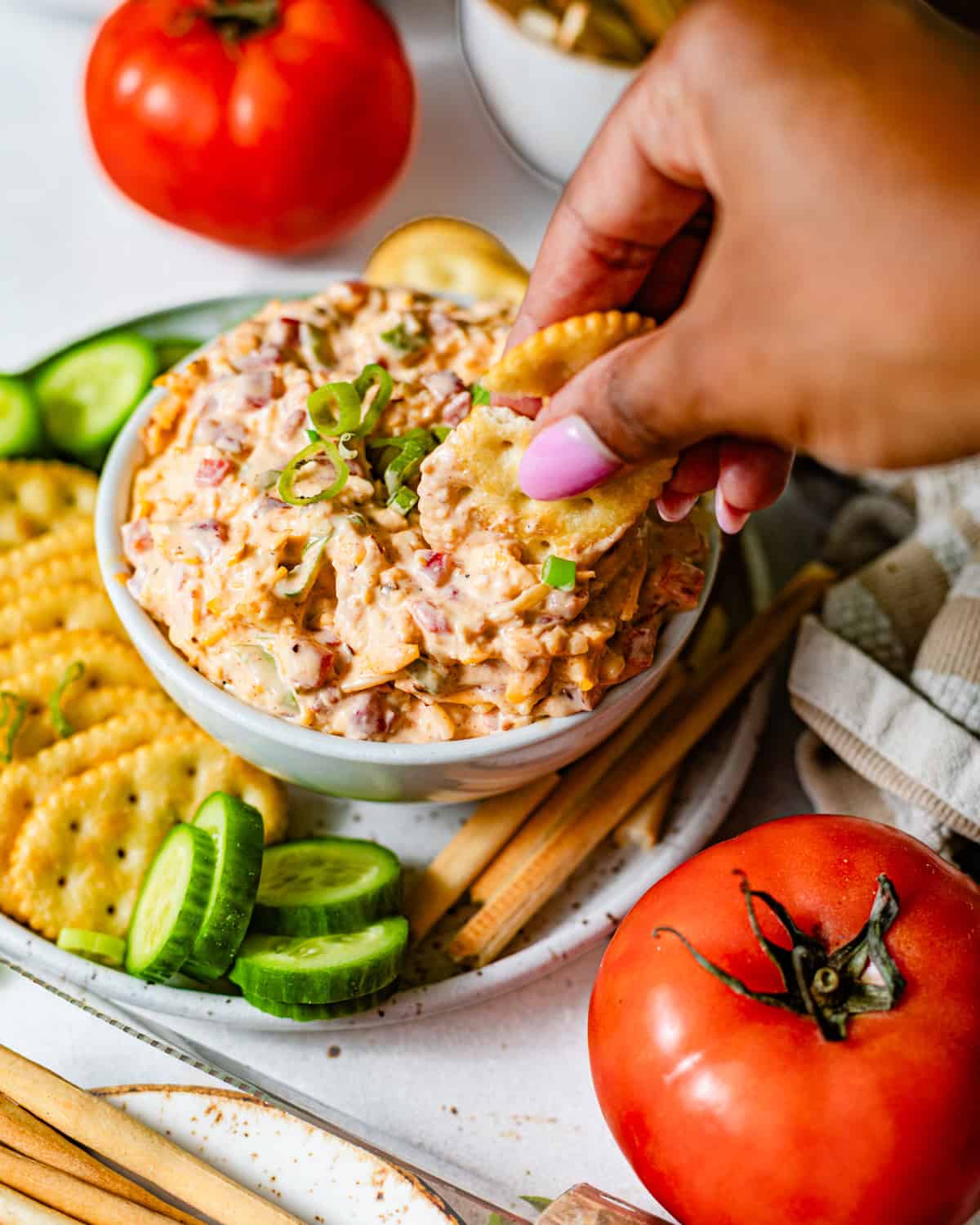 a hand dipping crackers into a bowl of pimento cheese.