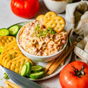 pimento cheese in a bowl surrounded by crackers, sliced cucumbers, and breadsticks.