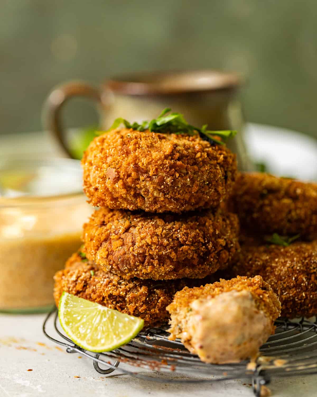 salmon croquettes stacked on top of each other on a wire rack with a lime wedges next to it.