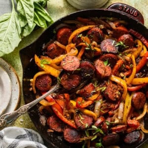 Smoked sausage, red and yellow bell peppers, and onions in a cast-iron skillet garnished with fresh parsley.