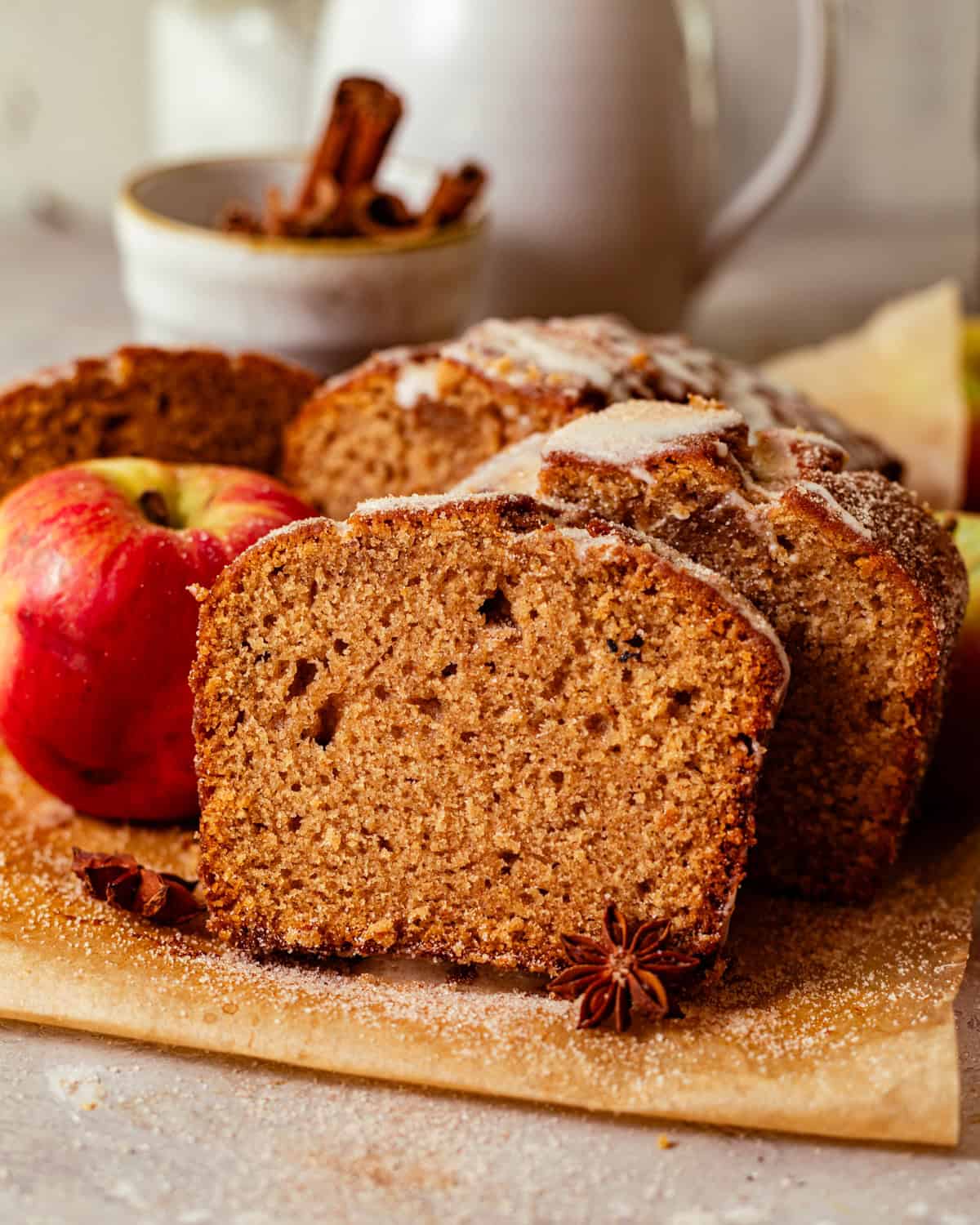 apple cider donut bread sliced on a piece of parchment paper placed next to an apple. 