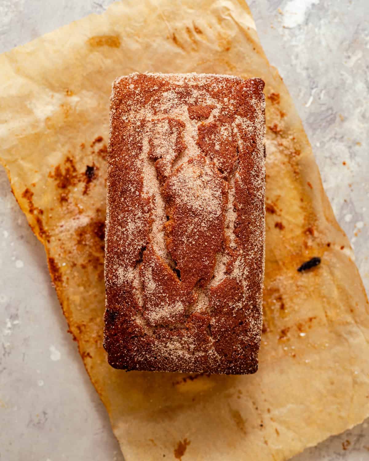 baked apple cider loaf on a piece of parchment paper covered in melted butter and sprinkled with cinnamon sugar.