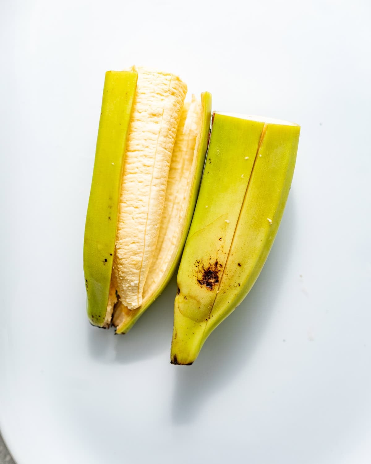 a plantain cut in half with a slit down the middle to make removing the skin easier.