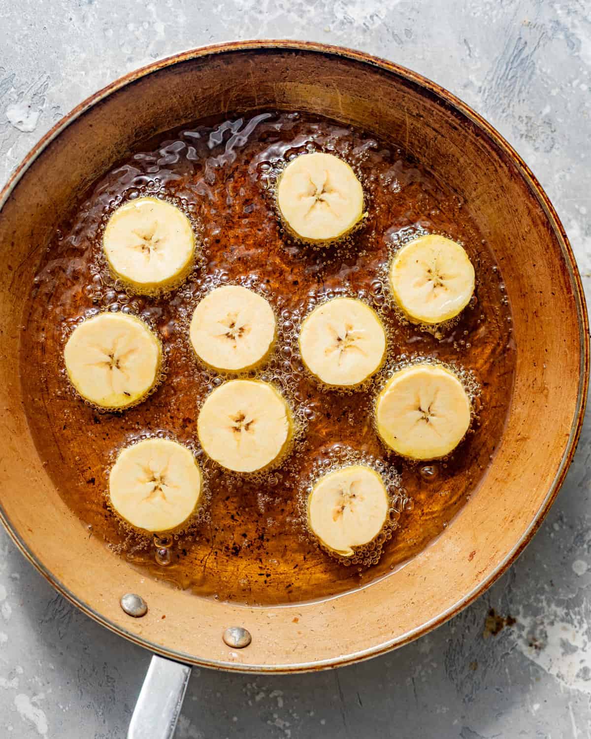 sliced plantains frying in a skillet.