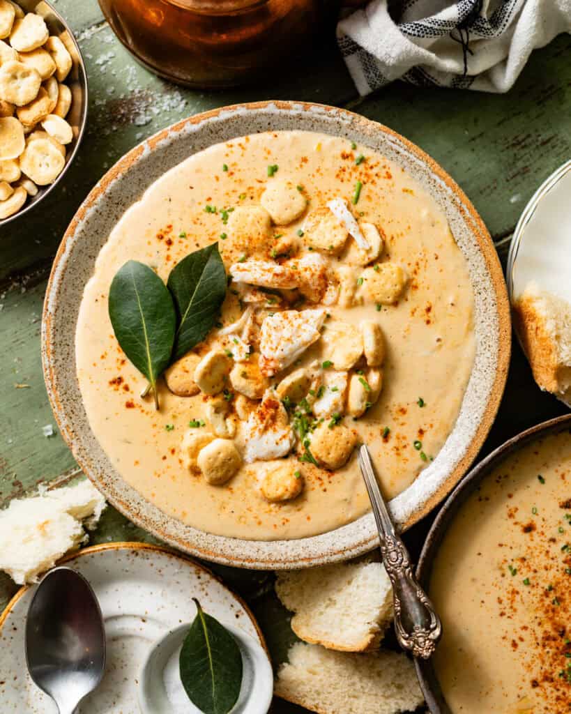 she crab soup in a bowl with a spoon topped with oyster crackers, jumbo lump crab, and a dash of old bay seasoning.