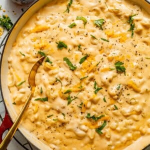 stovetop mac and cheese in a pot with a wooden spoon and garnished with parsley.