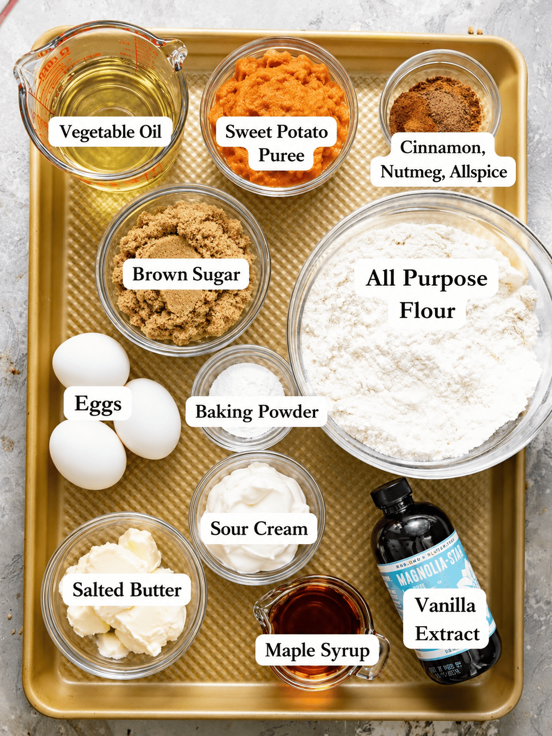 sweet potato coffee cake ingredients, including sweet potato puree, brown sugar, flour, eggs, sour cream, maple syrup, vegetable oil, and warm spices, arranged on a baking sheet with labels.
