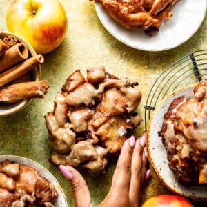 apple fritter donuts laid onto a flat surface with a hold grabbing one of the donuts.