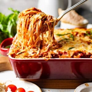 baked spaghetti in a baking dish with a serving spoon pulling a cheesy scoop out of the dish.