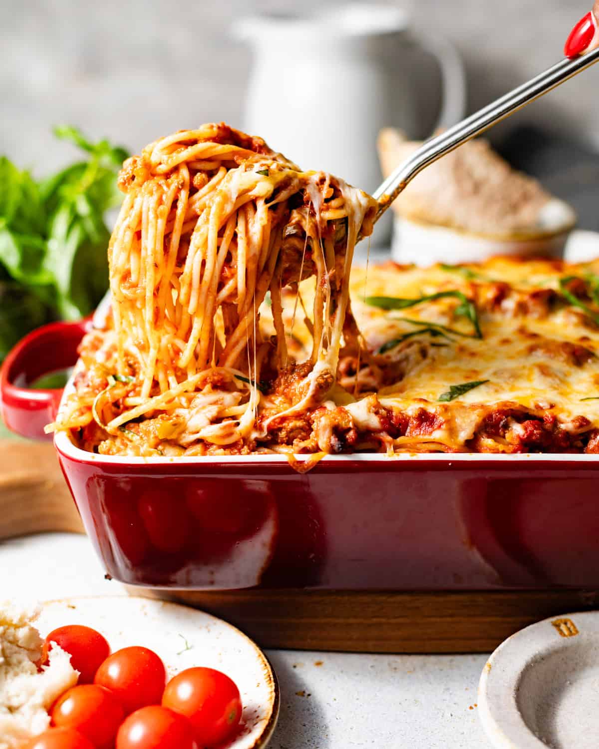 baked spaghetti in a baking dish with a serving spoon pulling a cheesy scoop out of the dish.