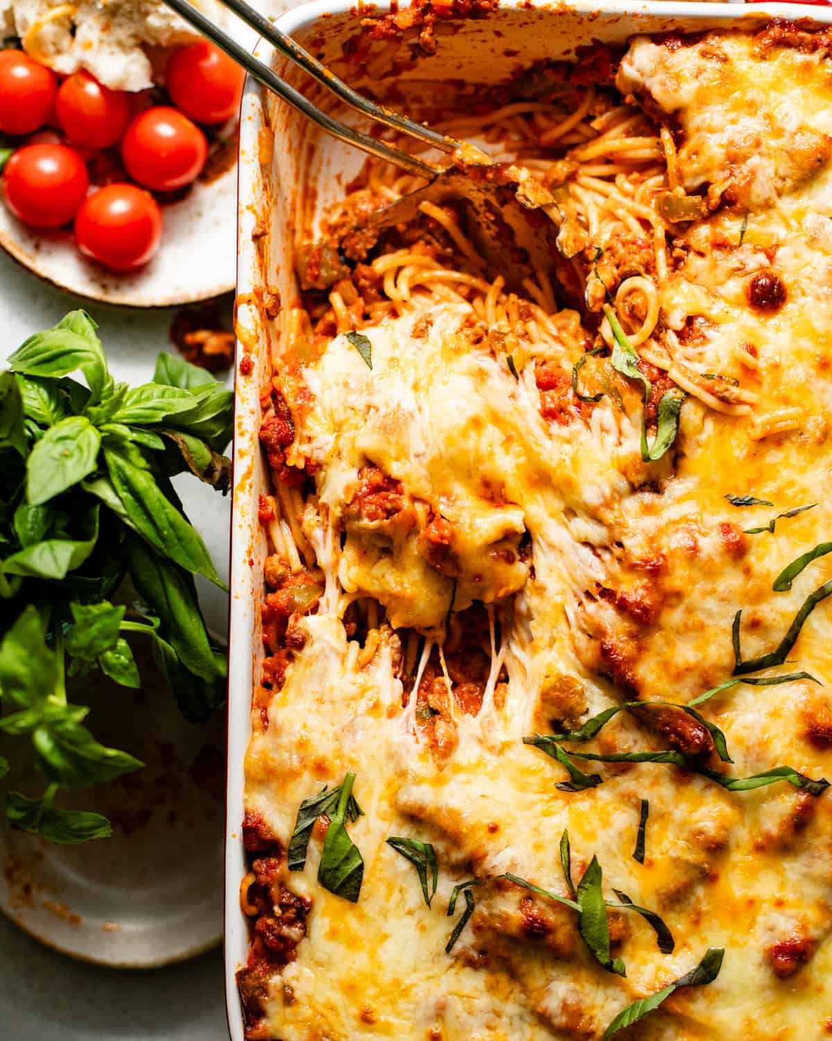 baked spaghetti in a baking dish with with a spoon scooping some of the spaghetti to show how cheesy and saucy the recipe is. 
