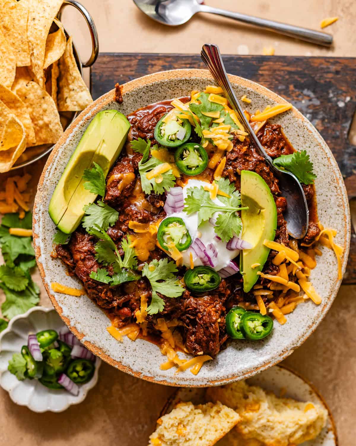 chuck roast chili in a bowl topped with cilantro, avocado, jalapenos, sour cream, red onion, and grated cheddar cheese.